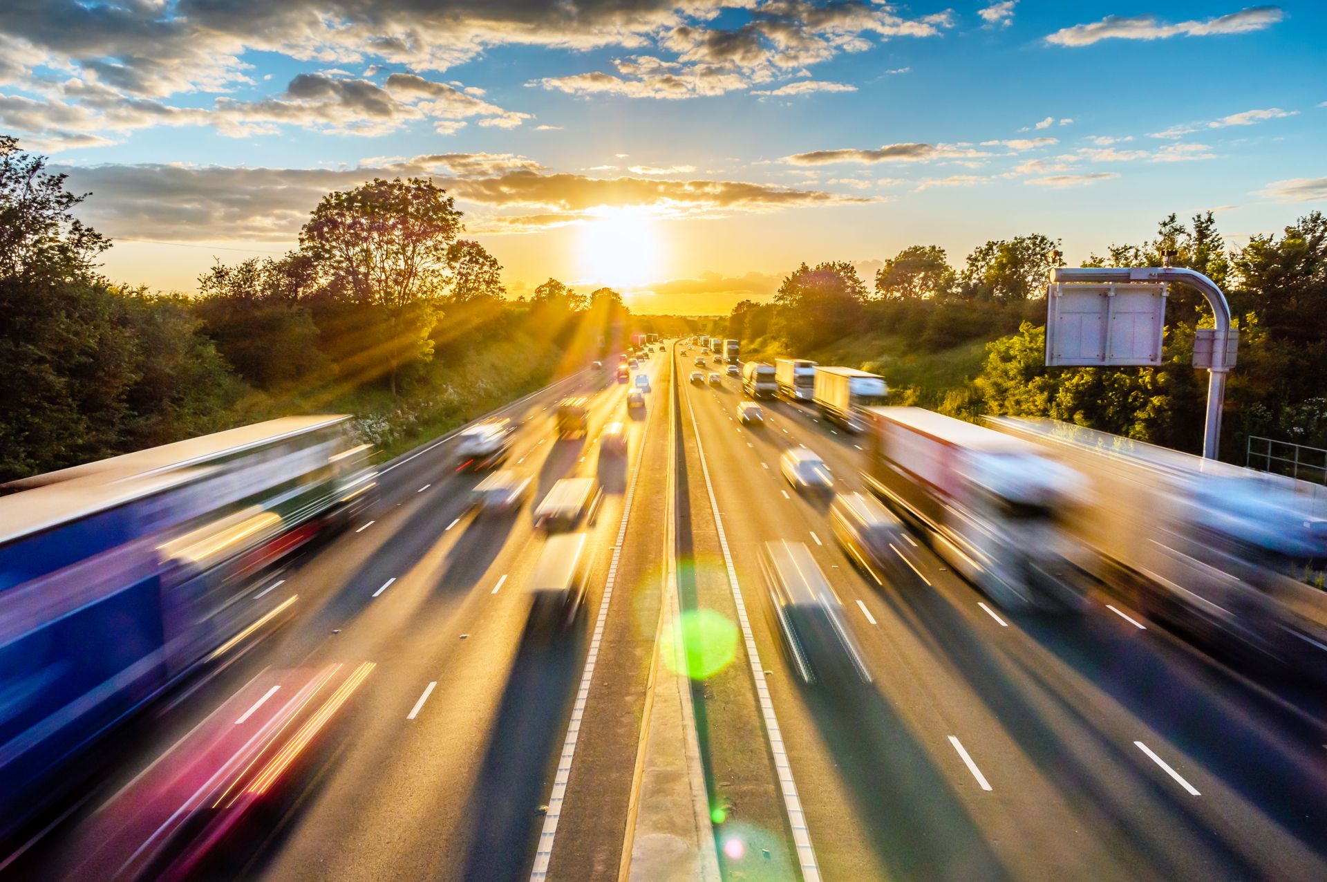 Verschwommene Autobahn mit Autos und Bäumen im Vordergrund.