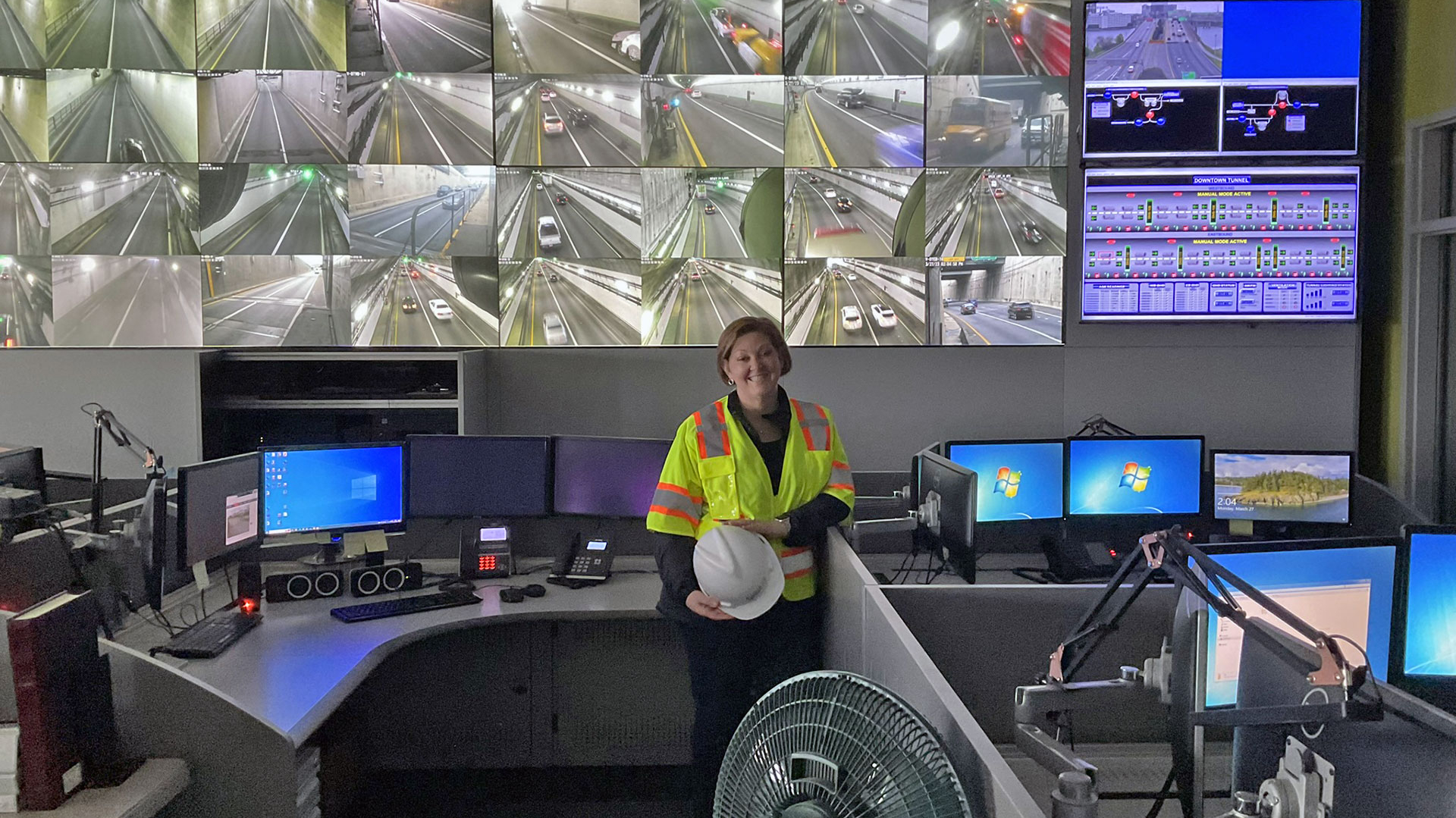 Frau in Sicherheitsweste steht vor einem großen Bildschirm.