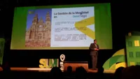 Ein Mann steht auf einer Bühne vor einer großen Leinwand und hält eine Präsentation.