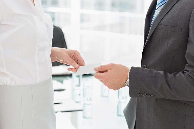 Un hombre entregando una tarjeta de visita a una mujer en un entorno formal de negocios.